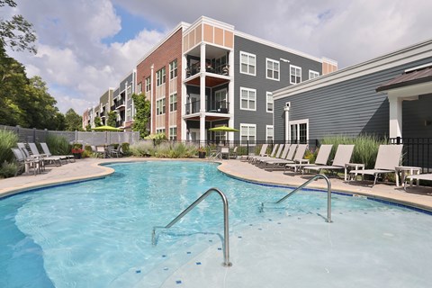 A swimming pool in front of a building with a fence and trees.