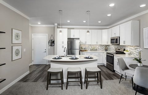 an open kitchen and living room with white cabinets and a round island with three chairs