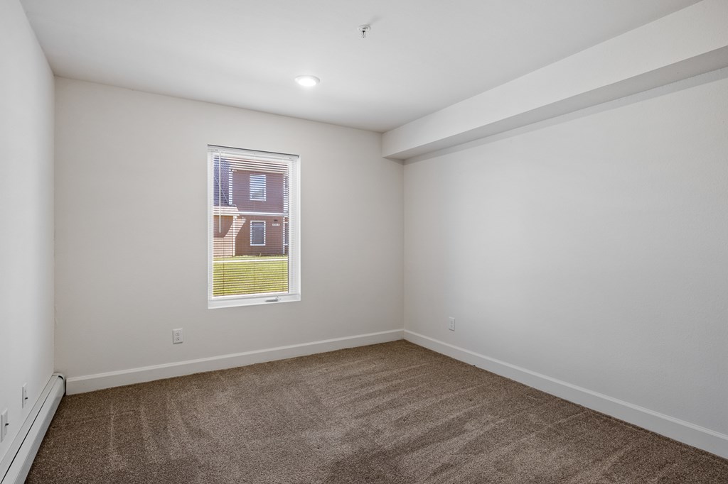 A room with a carpeted floor and a window showing a building outside.