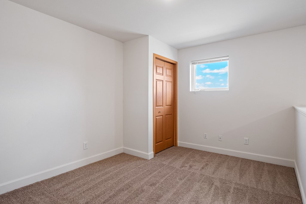 A room with a brown door and a window showing a blue sky with clouds.