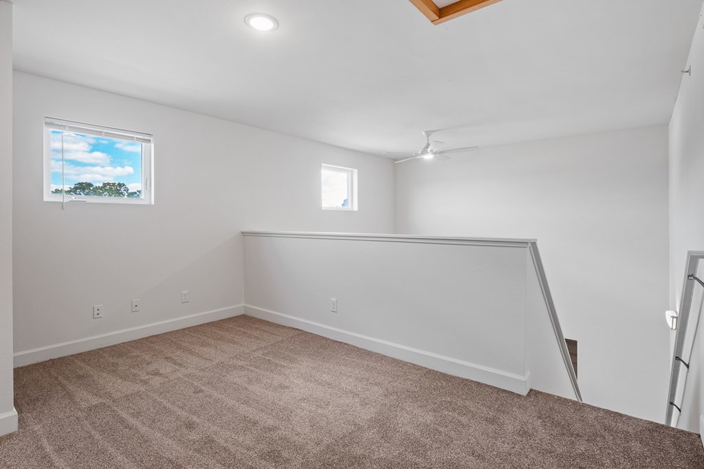 A room with a carpeted floor and a window showing a blue sky with clouds.