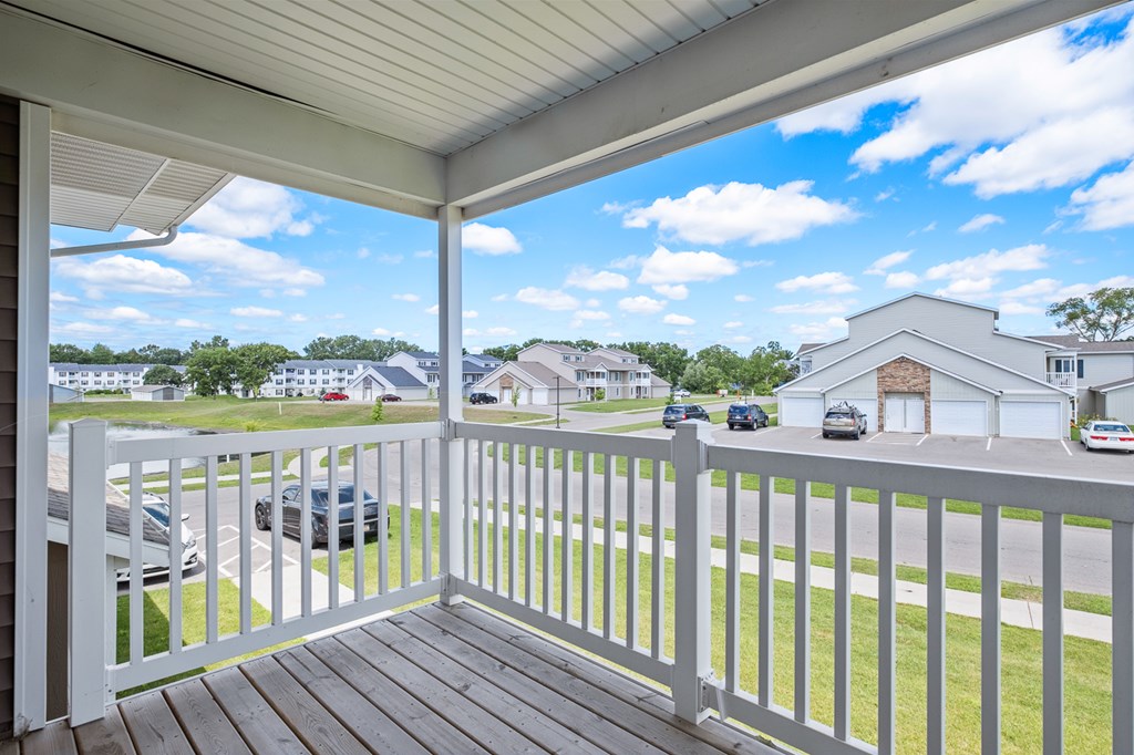 A white deck with a white railing overlooking a street with cars and houses.