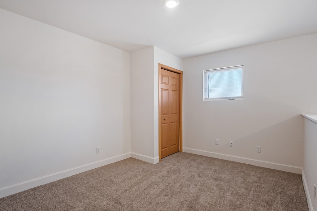 A room with a carpeted floor, a wooden door, and a window with blinds.