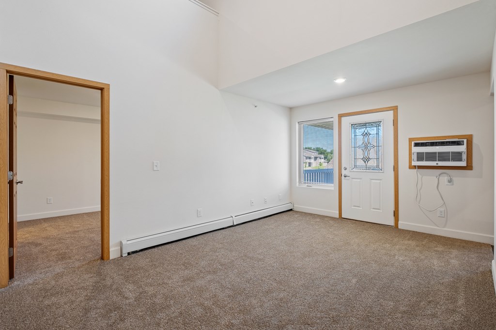 A room with a carpeted floor and a window with a view of a building outside.