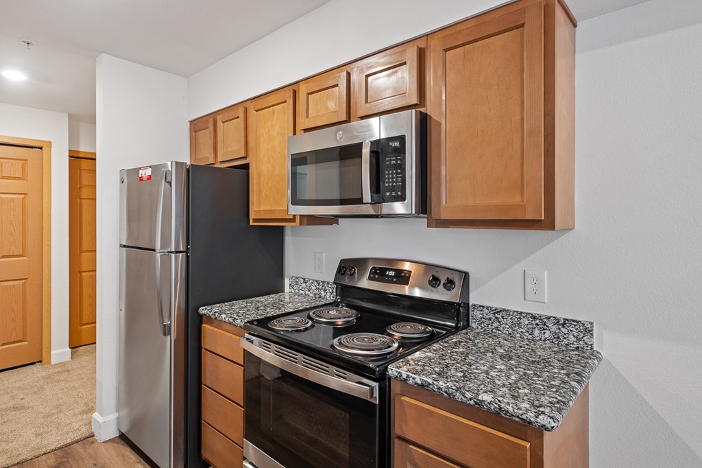 A kitchen with a black refrigerator, black stove, and wooden cabinets.