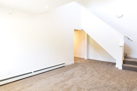 a living room with white walls and carpet and a staircase
