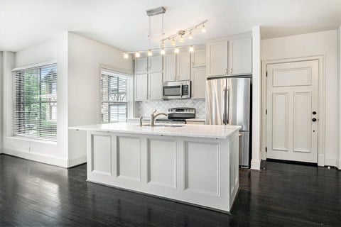 a white kitchen with a large island and stainless steel refrigerator