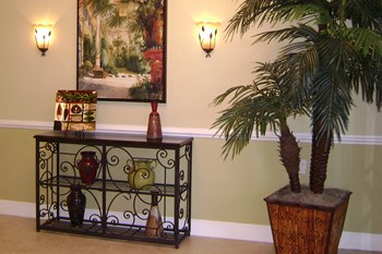 room with potted palm, small shelf with decor, painting and wall sconces