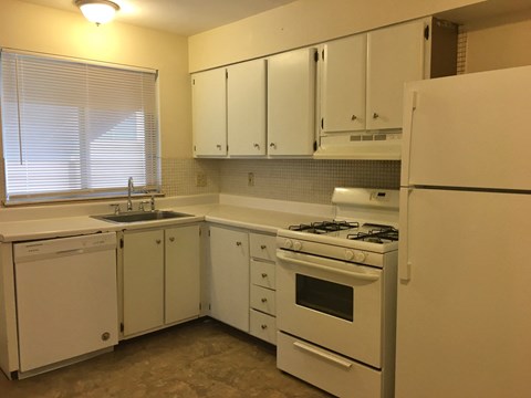A white kitchen with a stove, sink, and cabinets.