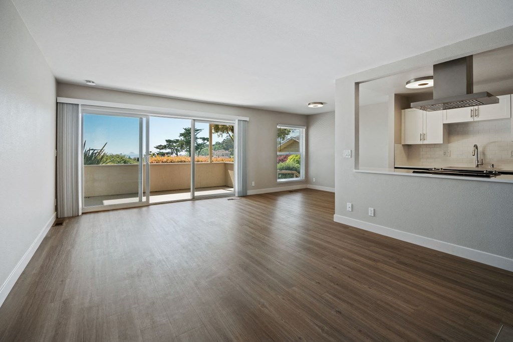 an empty living room with a kitchen and a balcony