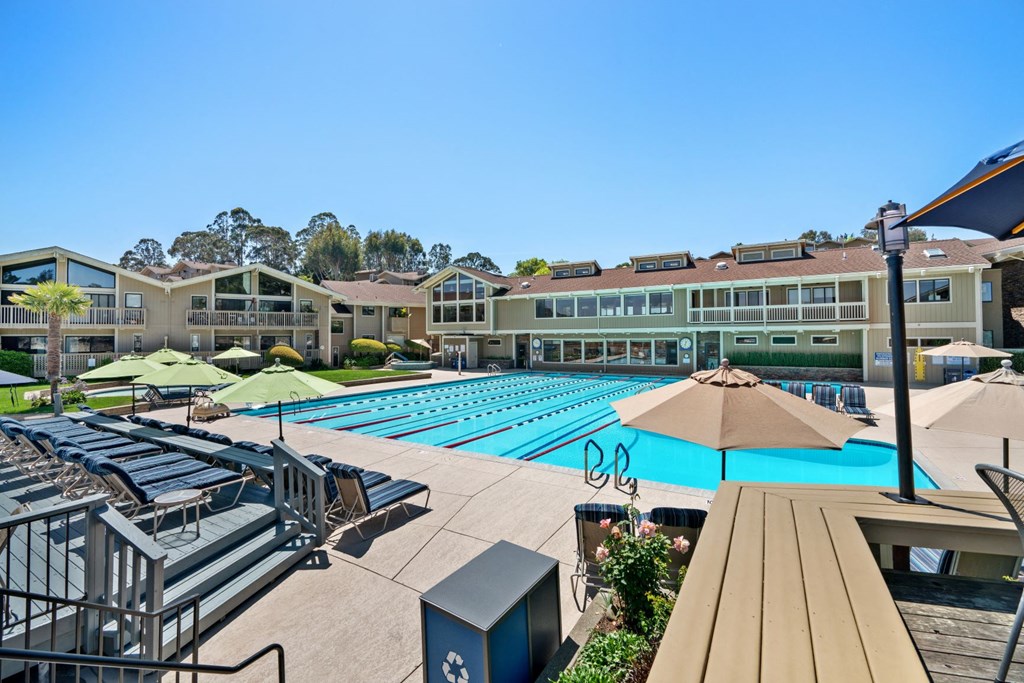 an aerial view of an outdoor pool with umbrellas and lounge chairs and buildings