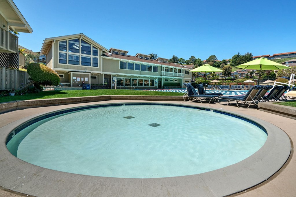 a resort style pool with chairs and umbrellas and a building in the background