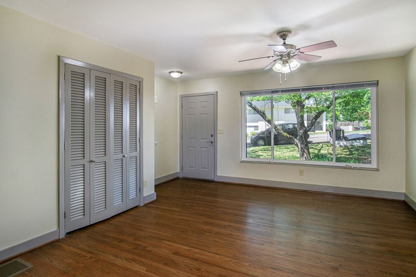an empty living room with a large window and a ceiling fan