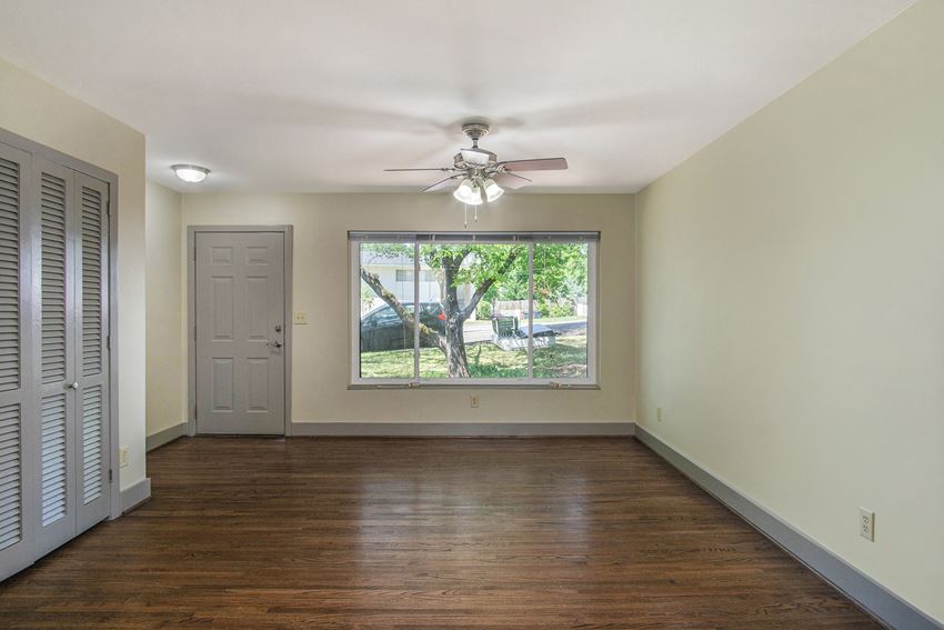 an empty living room with a large window and a ceiling fan