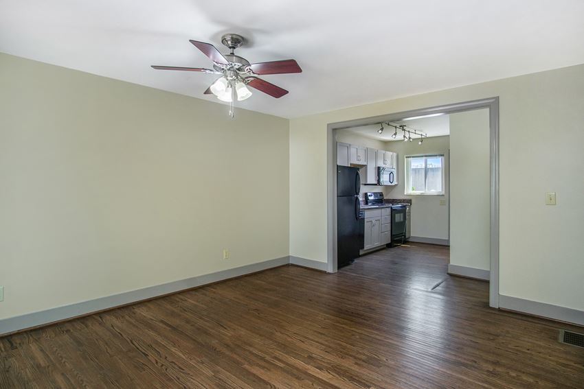an empty living room with a ceiling fan and a kitchen