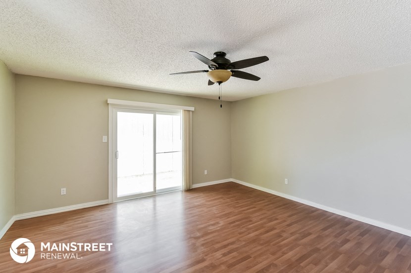 the spacious living room with wood flooring and a ceiling fan