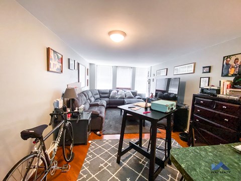 A living room with a couch, a chair, a bicycle, and a desk.