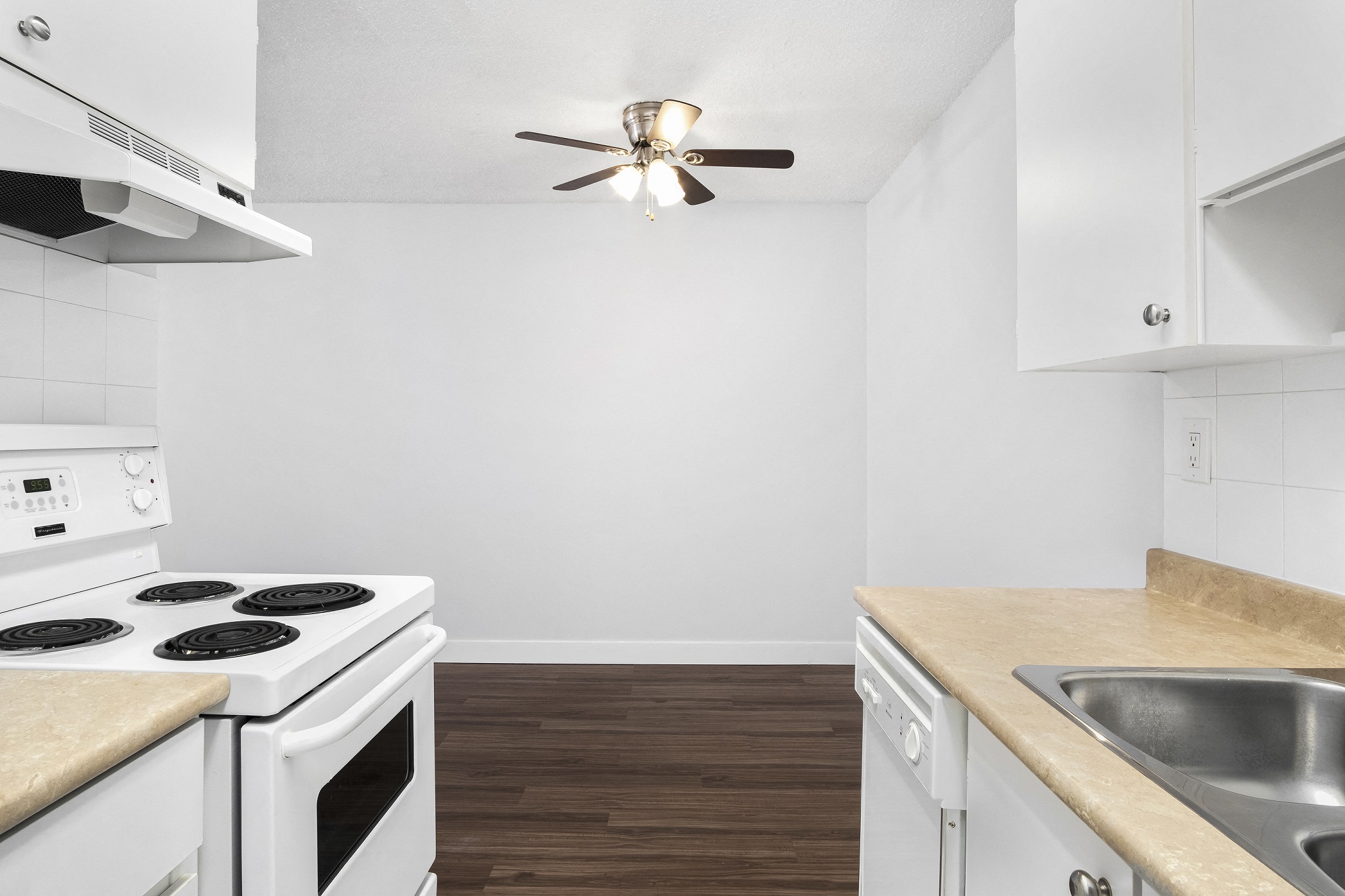 an empty kitchen with white appliances and a ceiling fan