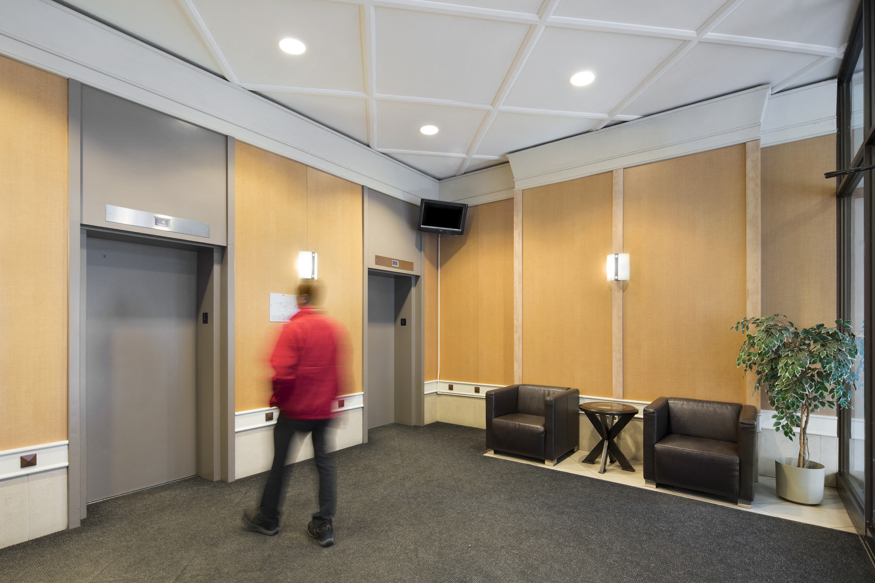 lobby with 2 chairs, an elevator and a person waiting for the elevator