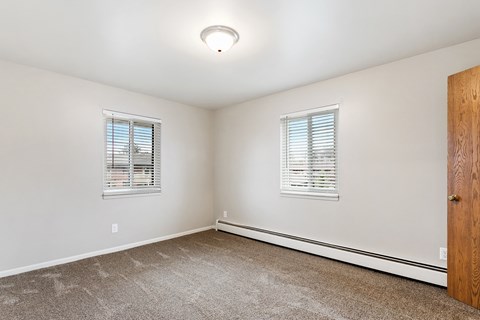 an empty room with carpet and two windows