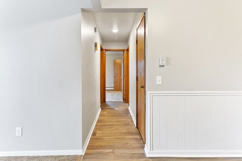 a hallway with white walls and wood flooring and a door to a bedroom