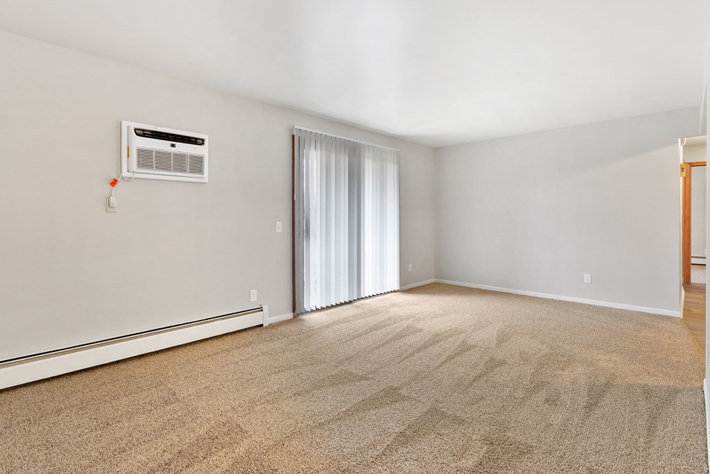 an empty living room with white walls and carpet and a sliding glass door