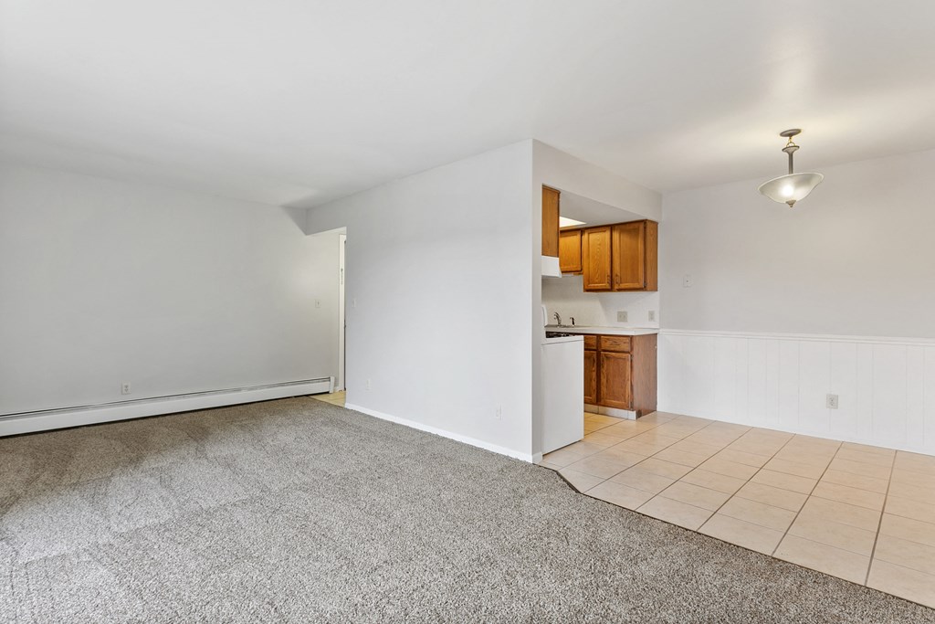 an empty living room with a kitchen in the corner