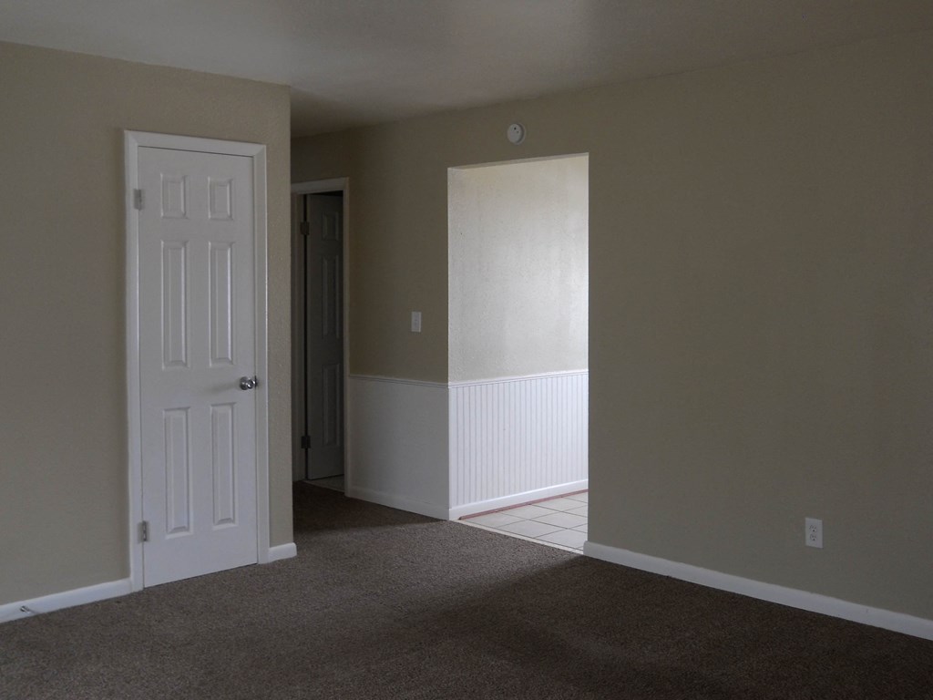 an empty living room with a white door and a hallway