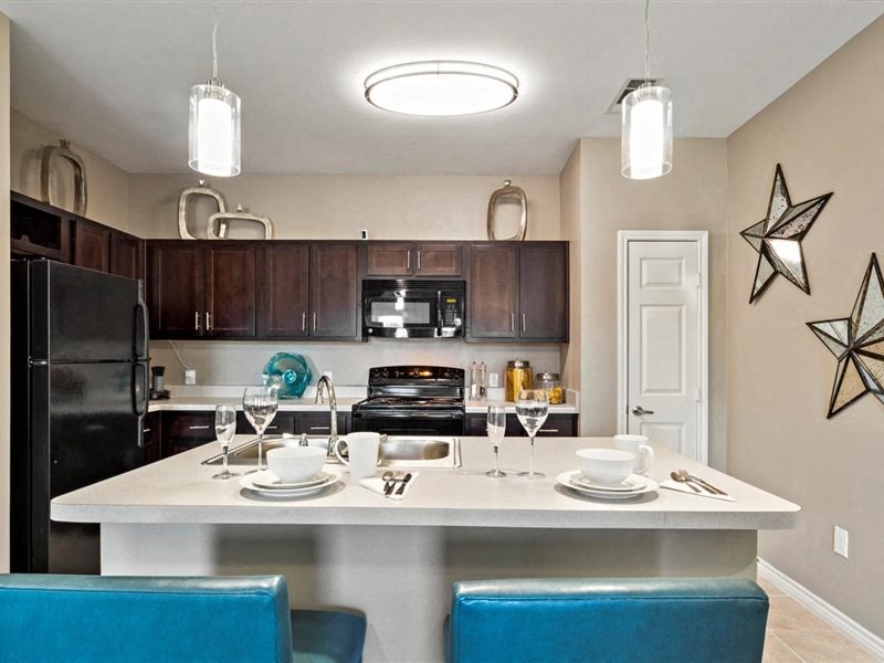 A kitchen with a table set for two and a black refrigerator.