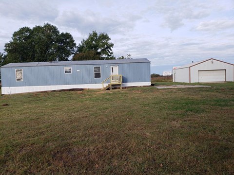 A blue building with a white door and windows sits in a grassy field.