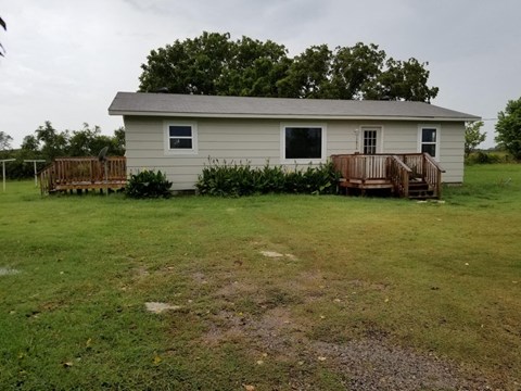 A small house with a porch and a tree in front.