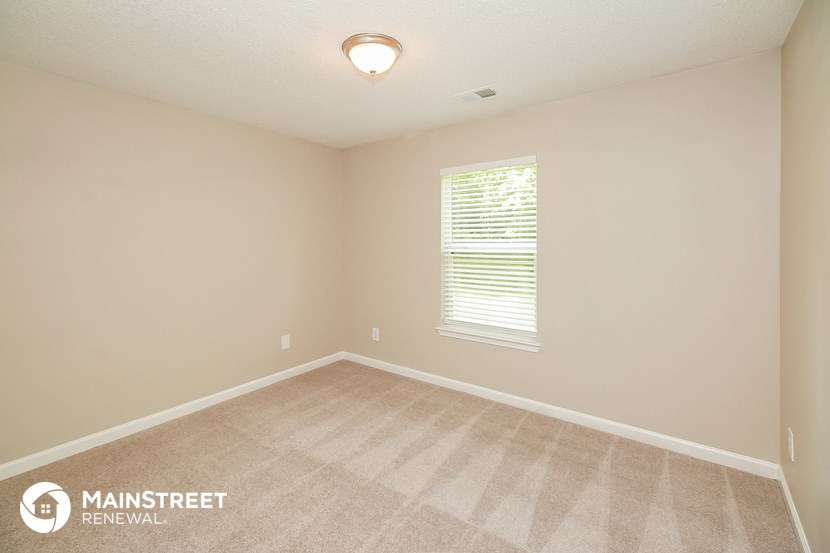 the spacious bedroom with carpeted flooring and a large window