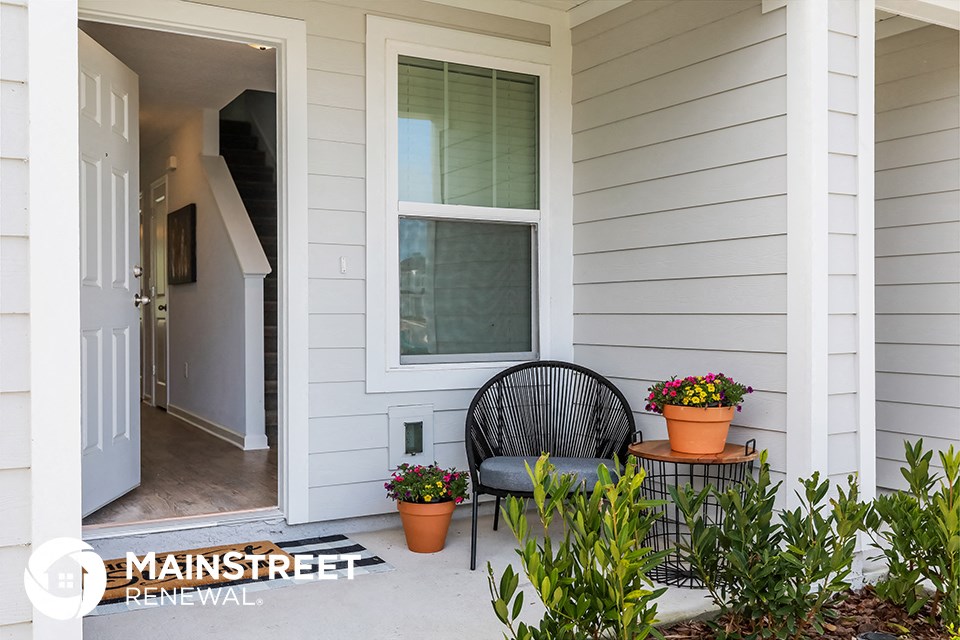 front porch of a white house with a black chair and potted plants