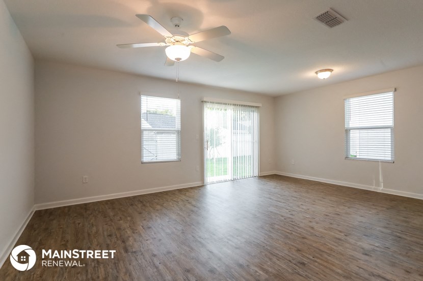 the spacious living room with wood flooring and a ceiling fan