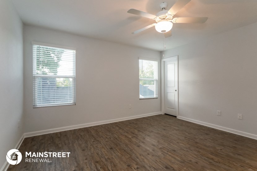 the spacious living room with wood flooring and a ceiling fan