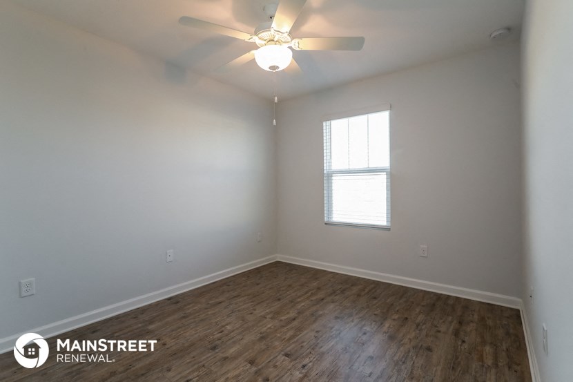 the spacious living room with wood flooring and a ceiling fan
