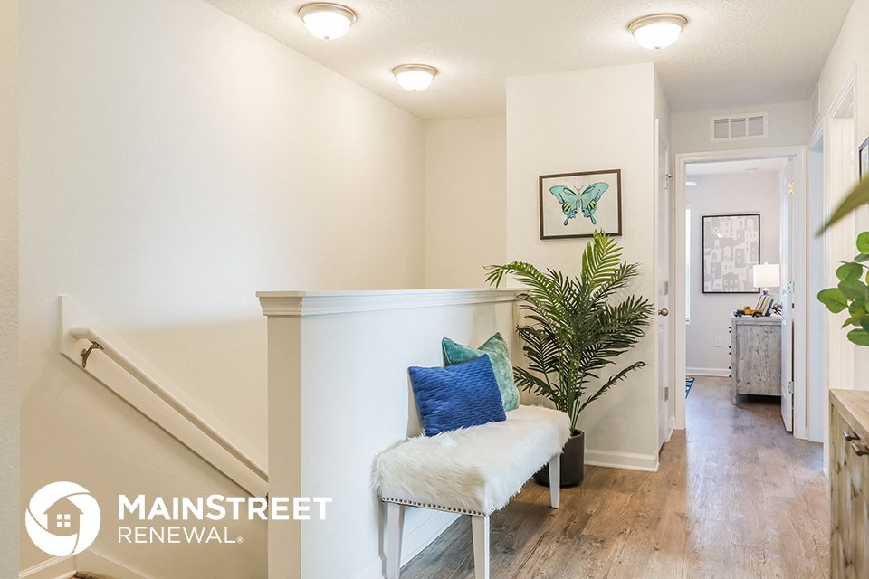 a living room with a white chair and a plant and a hallway with a staircase