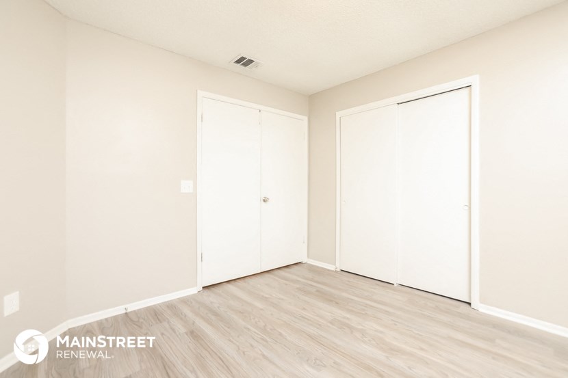 a master bedroom with two closets and a wood floor and white walls and doors