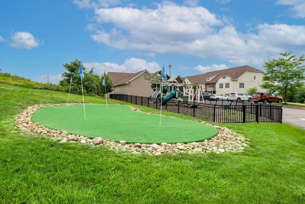 a putting green in a yard with a playground in front of a house