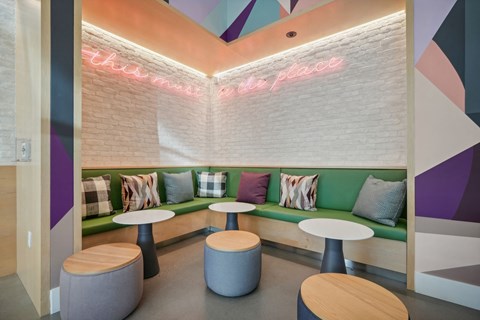 a lounge area with a green couch and tables and a neon sign