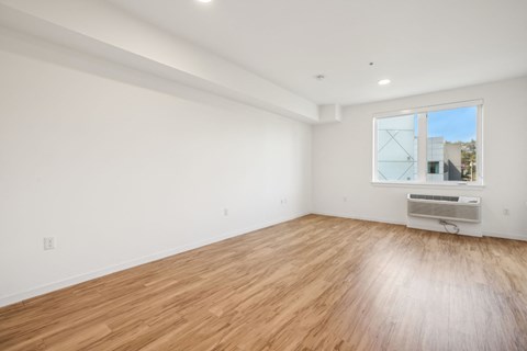 a living room with white walls and wood floors and a window