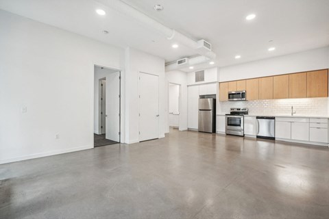 an empty living room with white walls and a kitchen with stainless steel appliances