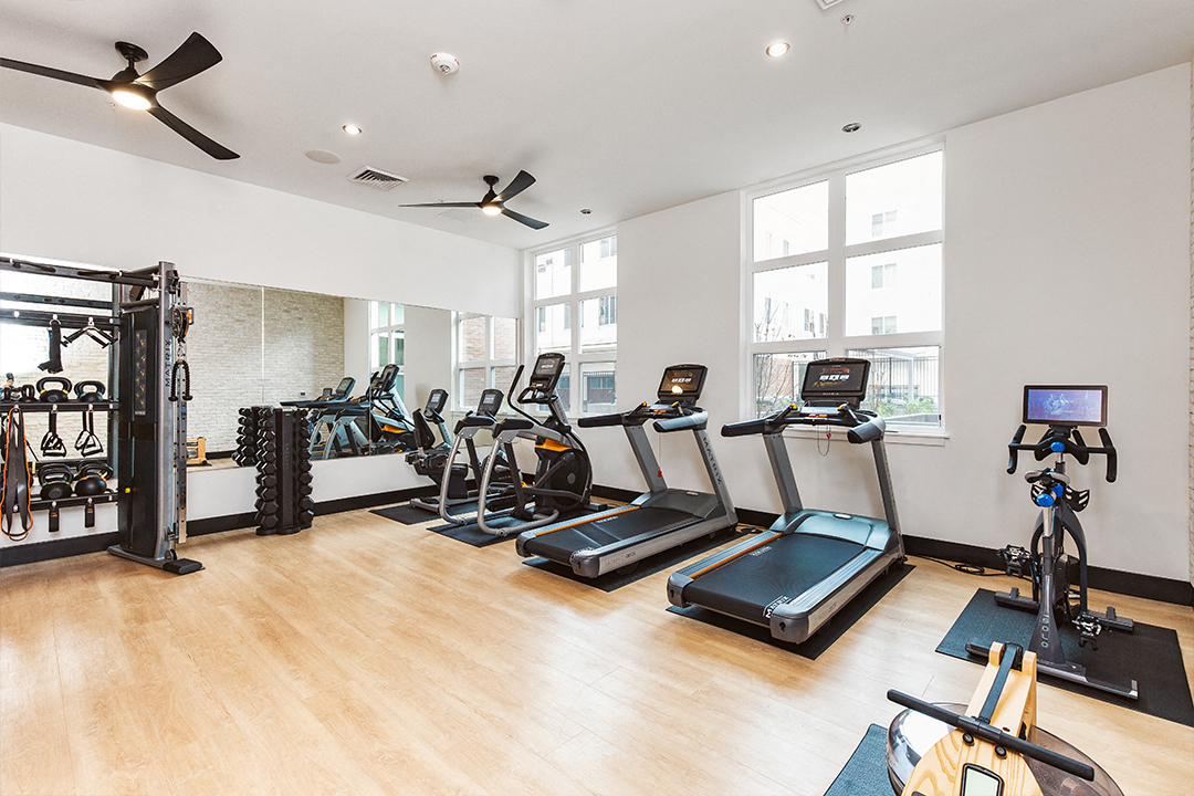 a gym with treadmills and other exercise equipment in a room with windows
