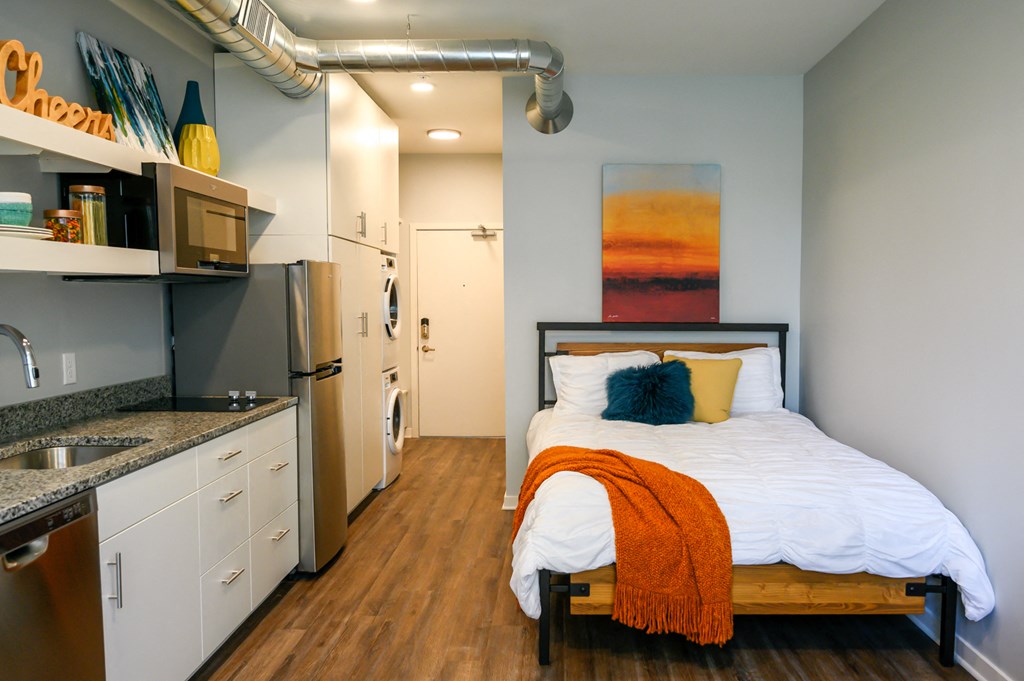 a bedroom in a small apartment with a bed and a kitchen