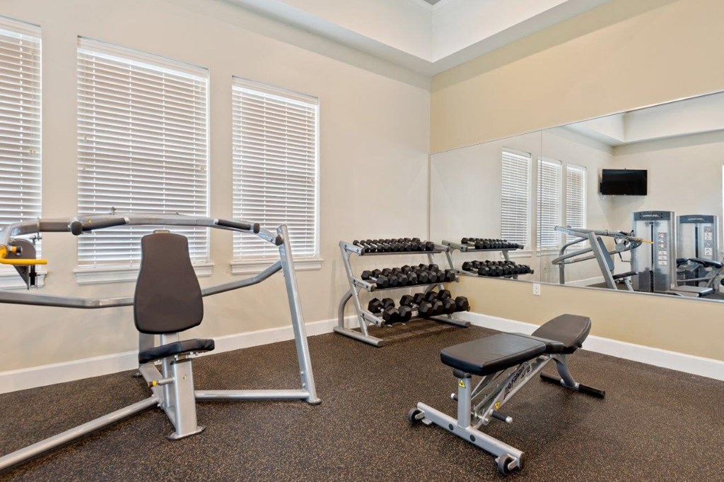 a gym with weights and a chair in a room with a mirror