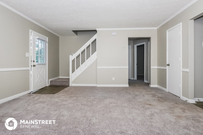 an empty living room with a staircase and a white door