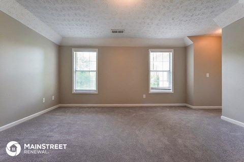 the living room of an apartment with carpet and two windows