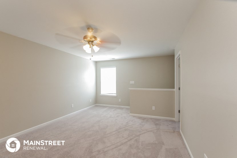 the spacious living room with ceiling fan and carpeting