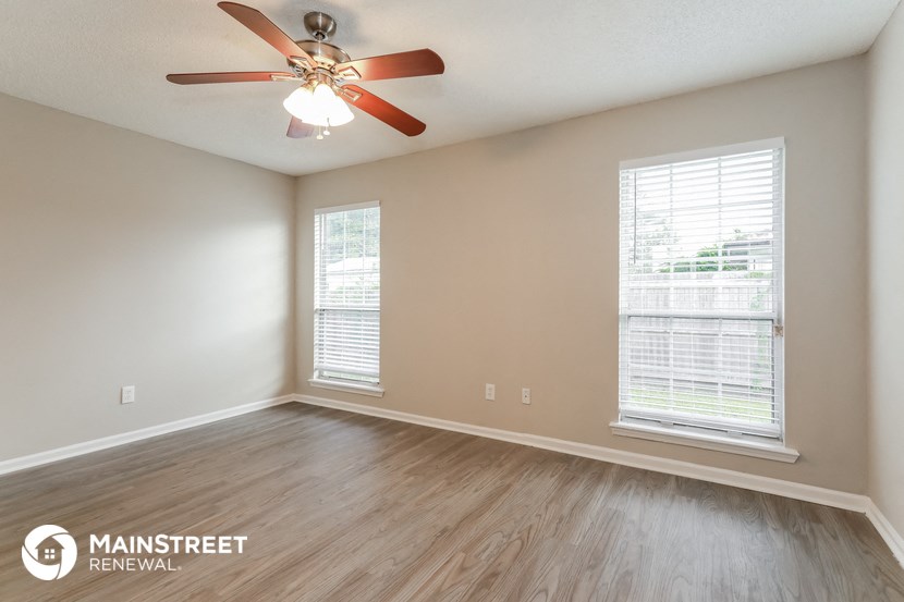 the spacious living room with wood flooring and a ceiling fan