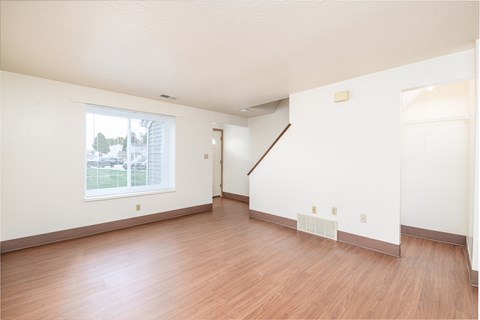 the living room and dining room of an apartment with wood flooring and a window